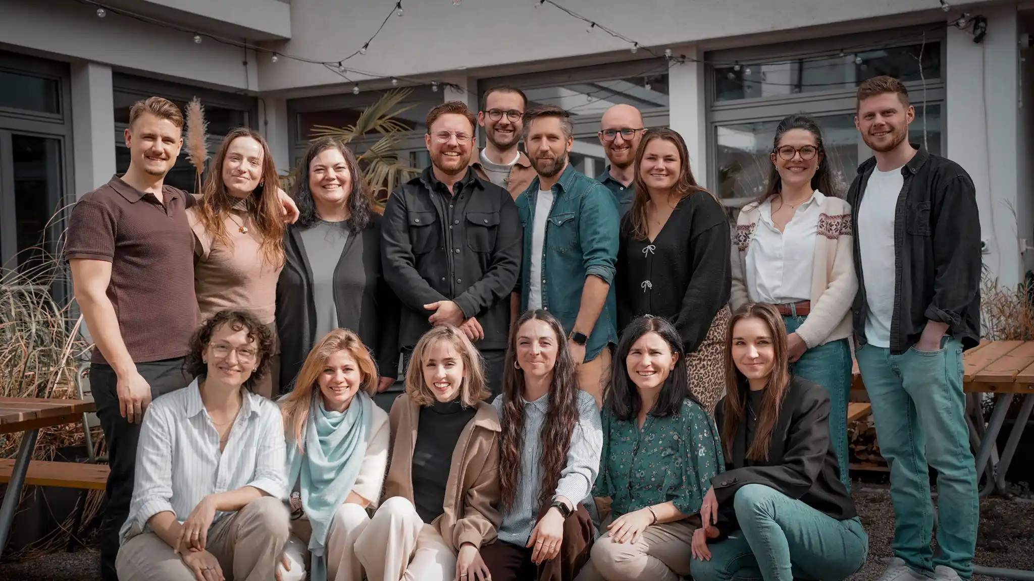 Capsule Hotel team smiling in outdoor courtyard, group portrait with string lights and wooden benches