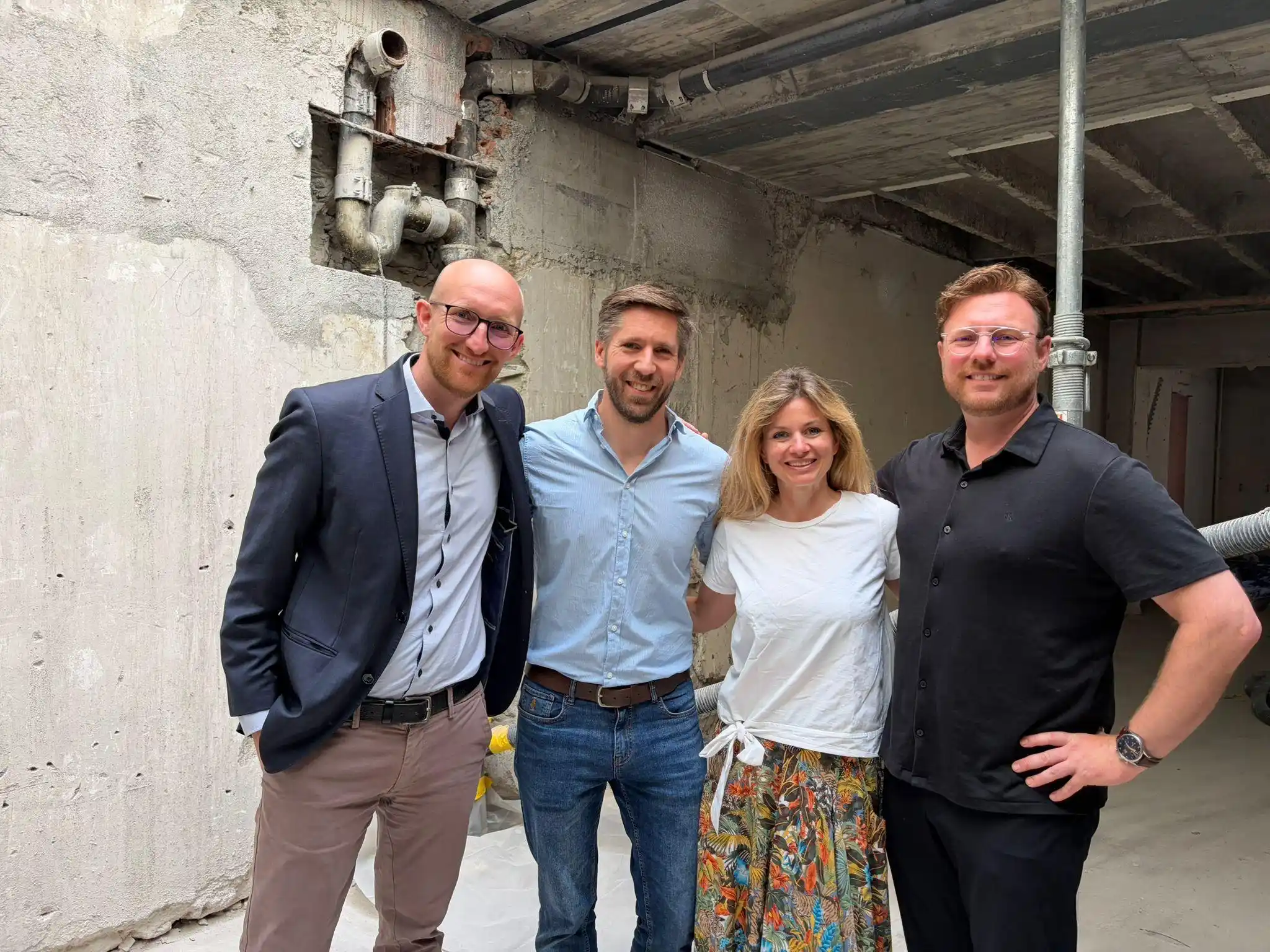 Capsule Hotel team of four smiling in an unfinished concrete space, site visit during renovation