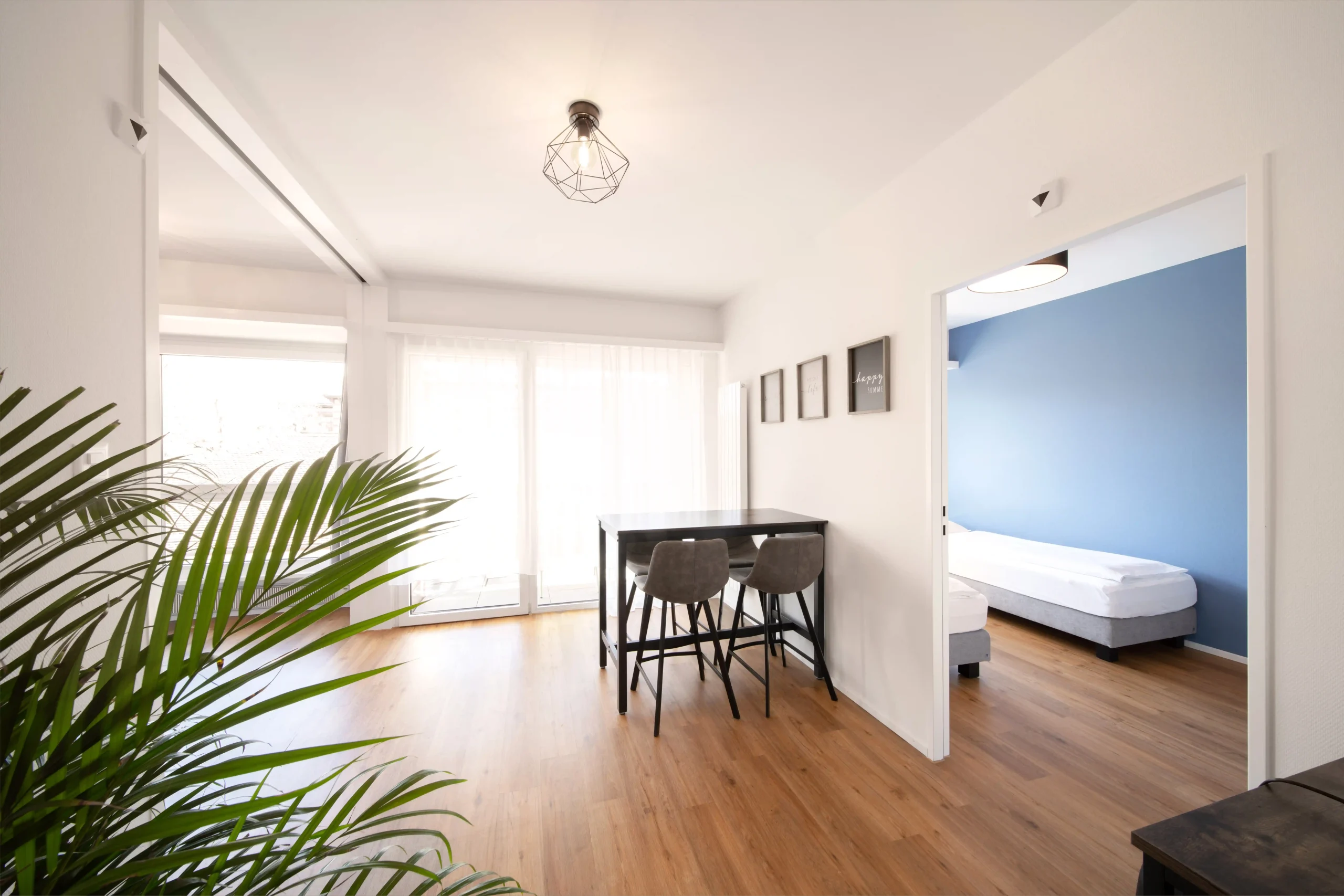 Modern apartment interior at Hyve Basel Capsule Hotel with wooden floor, table, chairs, and bedroom entrance.