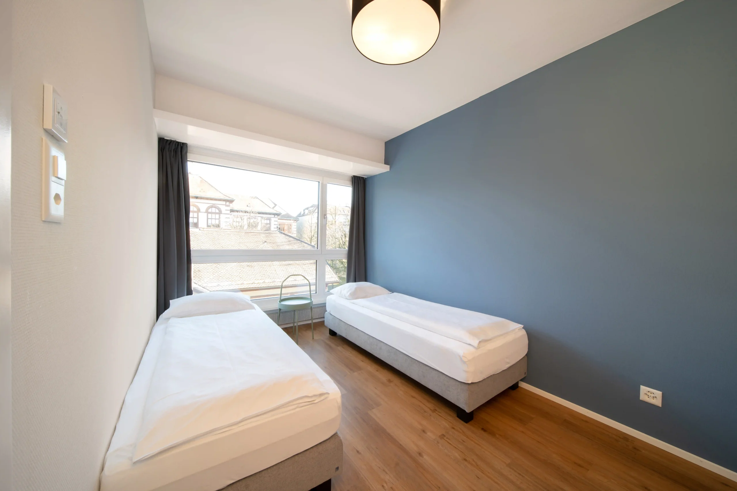 Two single beds in a dorm room with large window at Hyve Basel Capsule Hotel.