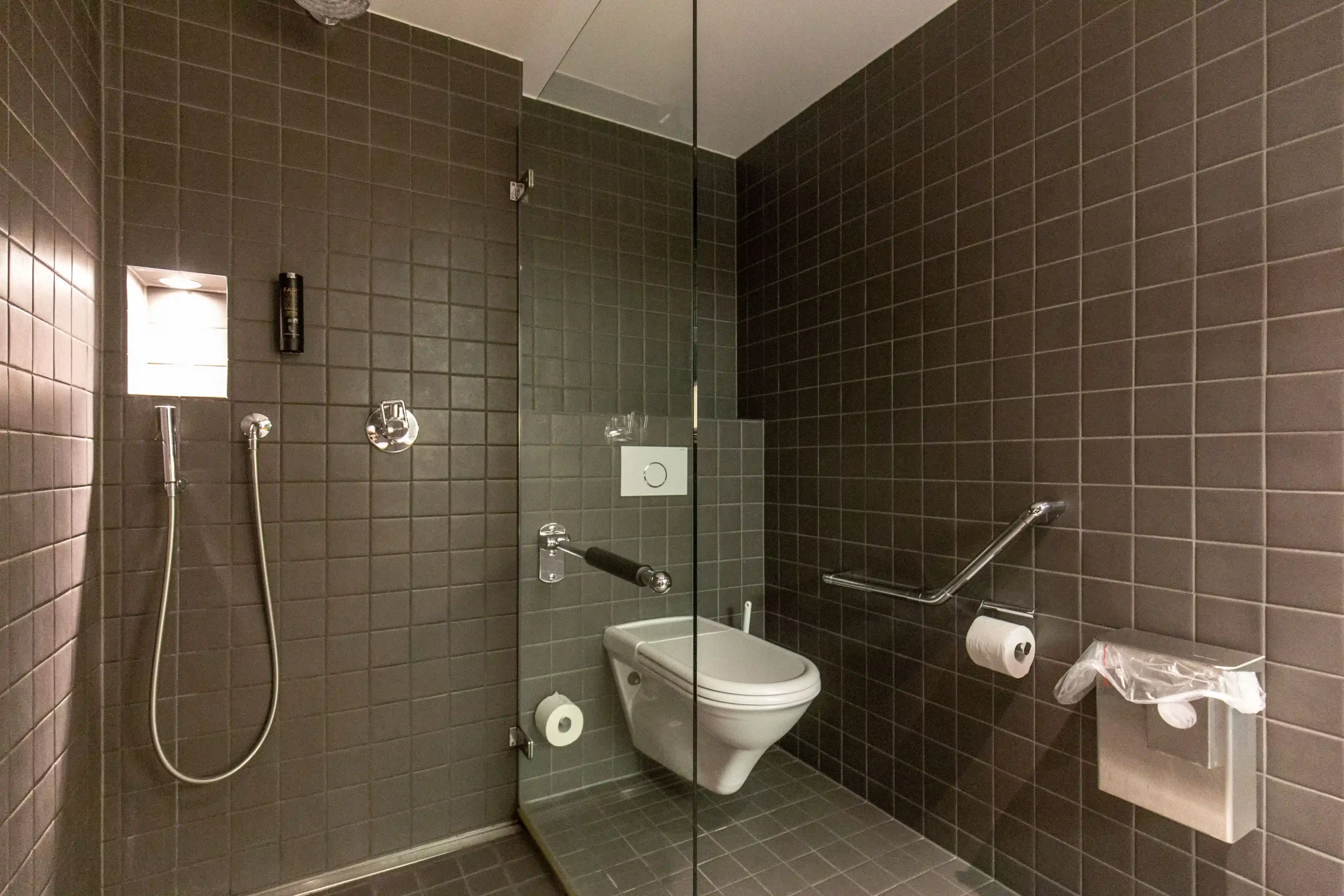 Modern bathroom with gray tiles and fixtures at Capsule Hotel, showcasing sleek, minimalist design and functionality.