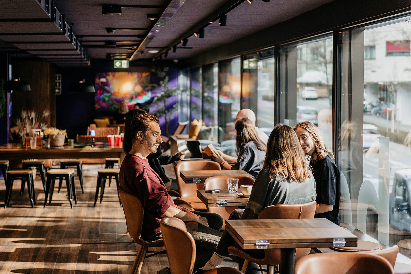Modern communal lounge area with guests at Capsule Hotel Lucerne Old Town, featuring large windows and stylish seating.