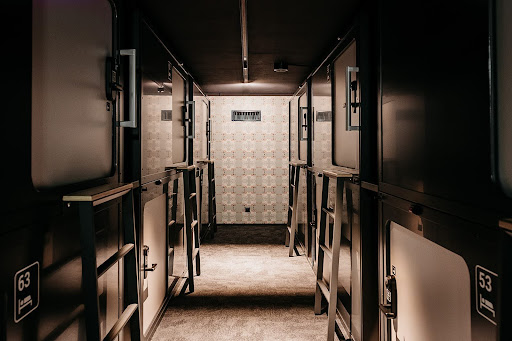 Capsule Hotel corridor with double-deck sleeping pods, ladders, and soft lighting in a sleek modern interior.
